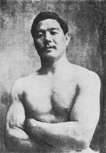 Studio portrait of Mitsuyo Maeda, bare-chested with arms folded, taken while he held the rank of fourth dan.